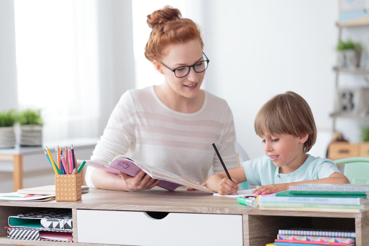 Red-headed female private tutor helping young student