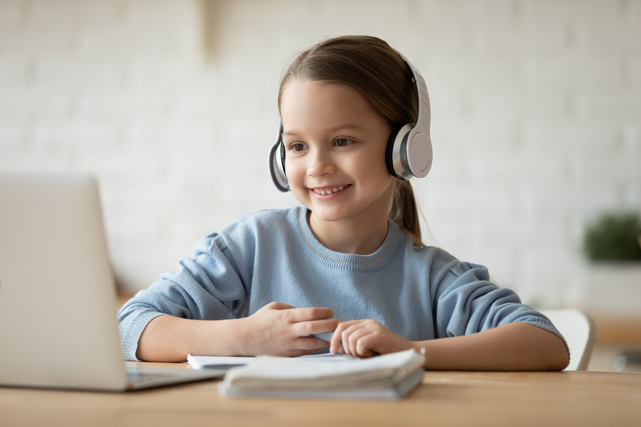 A young schoolgirl learning online with headphones on.