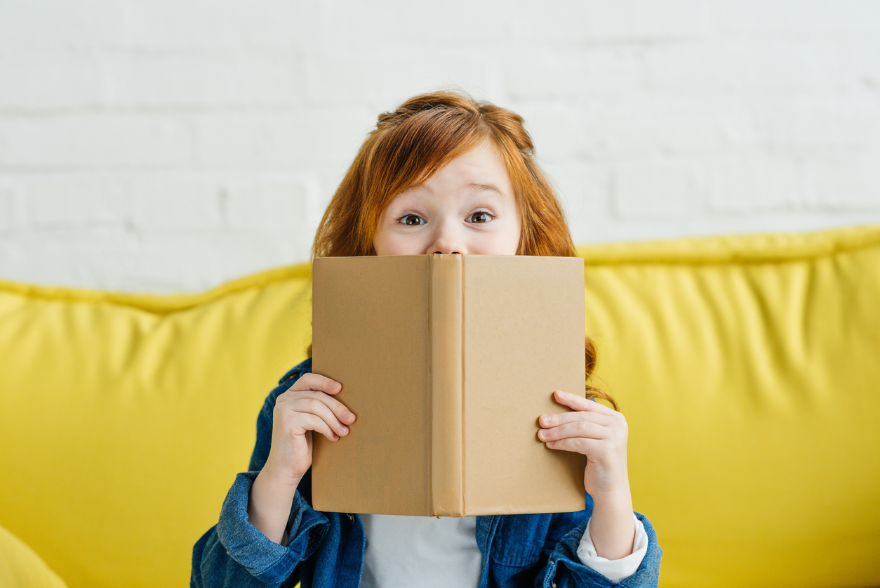 A red haired girl hiding behind a book